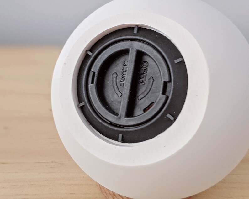 May include: White ceramic diffuser with a black plastic lid. The lid has a round opening with the words "OPEN" and "CLOSE" printed on it.