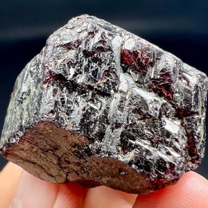 Pode incluir: Uma gema de cor vermelha escura, facetada, de corte bruto com um brilho metálico. A gema tem uma forma natural irregular.