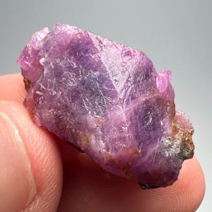 Puede incluir: Un cristal de rubí rosa vibrante con una forma geométrica multifacética. El cristal tiene una apariencia translúcida con un ligero tono púrpura.