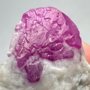 May include: A cluster of pink ruby crystals on a white matrix. The crystals are sharp and well-formed, with a glassy luster.