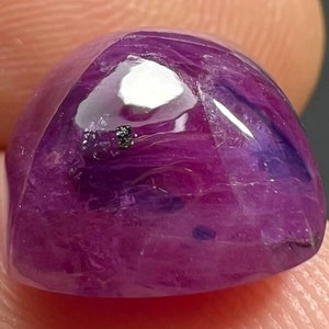 May include: A cabochon cut purple gemstone with a slightly domed shape. The stone has a translucent appearance with a hint of blue.