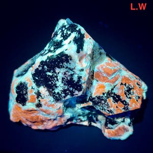 May include: A close-up of a rock formation with a mix of colours. The rock has a base of orange and white, with large patches of black. The rock is illuminated with a blue light, and the text "L.W" is in the upper right corner.