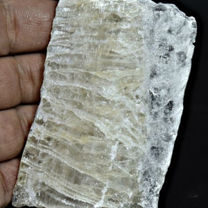 Puede incluir: Una gran pieza de cristal de selenita rectangular, blanca, translúcida, toscamente labrada, con estrías visibles.