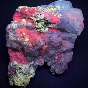 May include: A large, irregularly shaped rock with a purple, pink, and white crystalline structure. The rock has a rough, textured surface and appears to be illuminated by a UV light, causing the crystals to fluoresce.