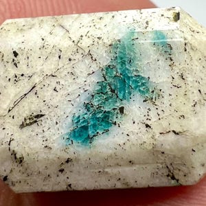 May include: A white and green gemstone with a faceted cut. The gemstone has a unique pattern of green inclusions.