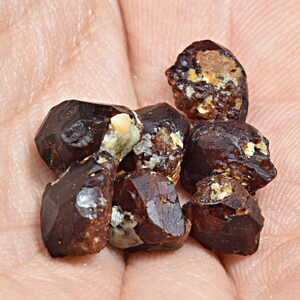 May include: A group of dark red, brown, and black crystals with a rough, textured surface. The crystals are clustered together and have a natural, earthy appearance.