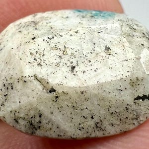 May include: A white oval cabochon gemstone with black flecks and a slightly iridescent sheen.