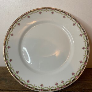 May include: White porcelain plate with a gold and black floral border. The border features pink flowers and green leaves.