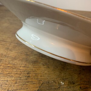 May include: A white ceramic serving dish with a gold rim. The dish has a pedestal base and is designed for serving food.