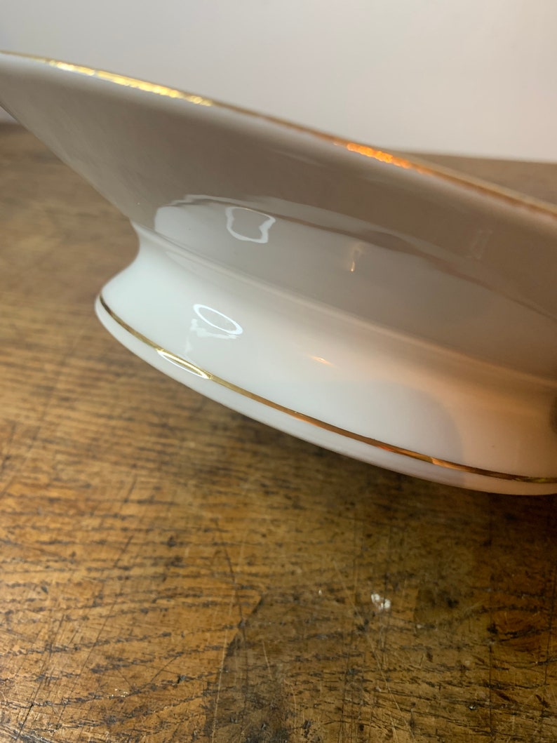 May include: A white ceramic serving dish with a gold rim. The dish has a pedestal base and is designed for serving food.