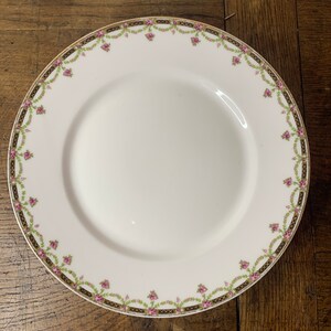 May include: A white porcelain plate with a gold and green floral border. The plate features a delicate floral design with pink flowers and green leaves.