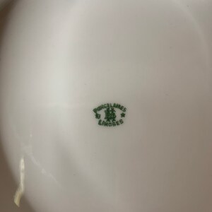 May include: A close-up of a white porcelain plate with a green mark that reads "Porcelaines Limoges" with a crown and two stars.