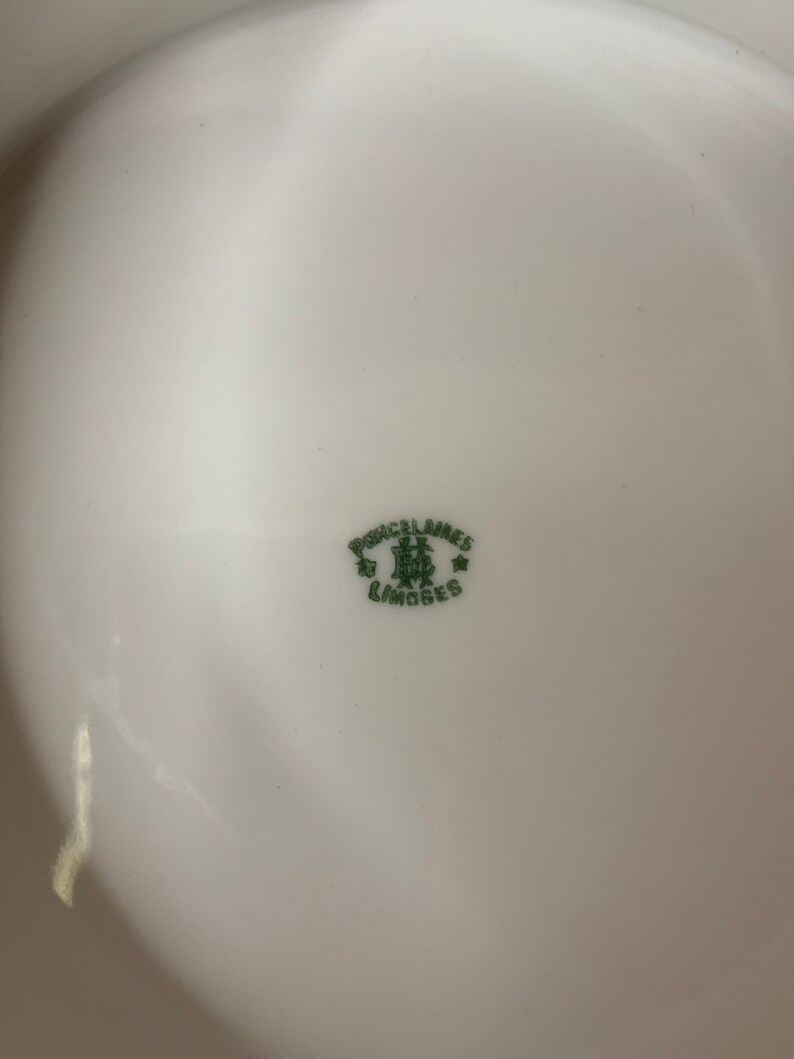 May include: A close-up of a white porcelain plate with a green mark that reads "Porcelaines Limoges" with a crown and two stars.