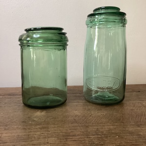 Peut inclure: Deux bocaux en verre vert avec des couvercles. Le plus grand bocal a le mot "SILCEA" en relief sur le côté.