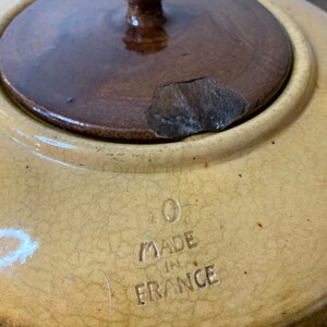 K&ouml;nnte beinhalten: Ein antiker Keramiktopf mit einem Holzdeckel. Der Topf ist gelb mit einer craquel&eacute;-Glasur und tr&auml;gt die Aufschrift "Made in France" auf dem Boden.