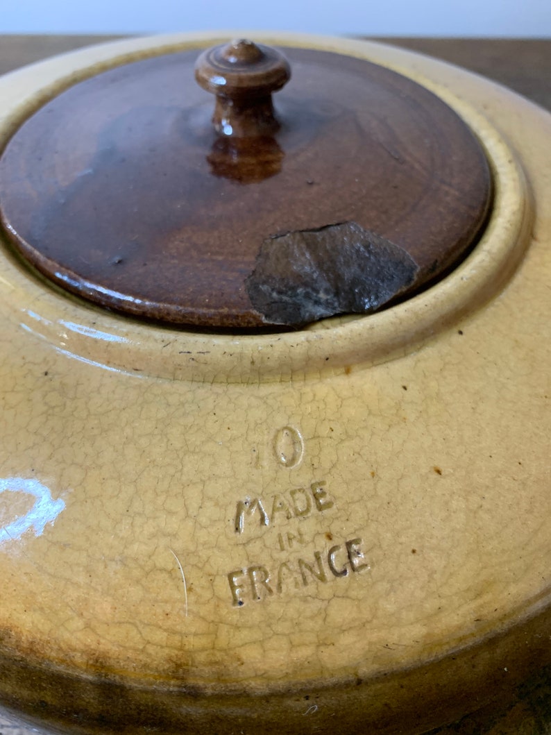 K&ouml;nnte beinhalten: Ein antiker Keramiktopf mit einem Holzdeckel. Der Topf ist gelb mit einer craquel&eacute;-Glasur und tr&auml;gt die Aufschrift "Made in France" auf dem Boden.