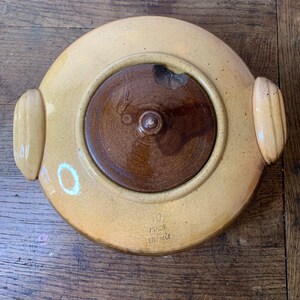 K&ouml;nnte beinhalten: Eine gelbe Keramik-Auflaufform mit einem braunen Deckel und zwei Griffen. Die Form hat eine wei&szlig;e Aufschrift mit der Aufschrift "Made in France".