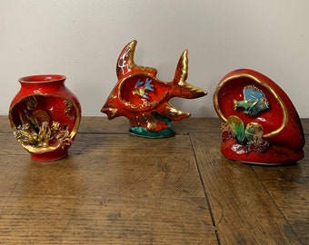 Può includere: Tre figurine in ceramica rossa con dettagli dorati che raffigurano pesci e coralli. Le figurine sono su una superficie di legno.