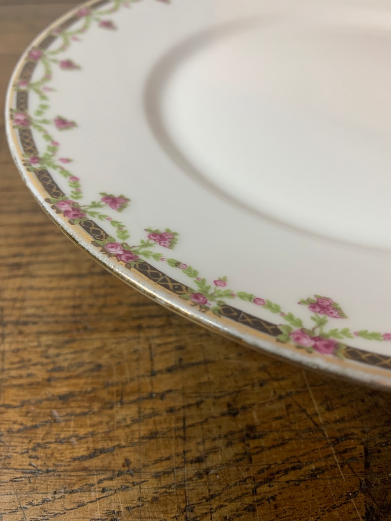 May include: A white porcelain plate with a gold rim and a delicate floral design featuring pink roses and green leaves.