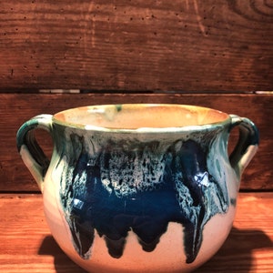 Peut inclure: Un pot en céramique blanche avec un glaçage bleu et vert. Le pot a deux anses et une forme arrondie.