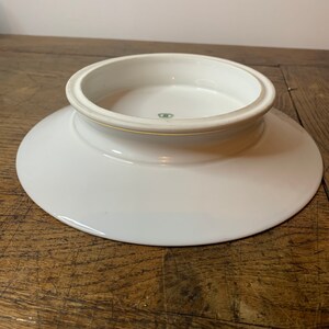 May include: White ceramic pedestal plate with a raised centre and a green mark on the bottom.