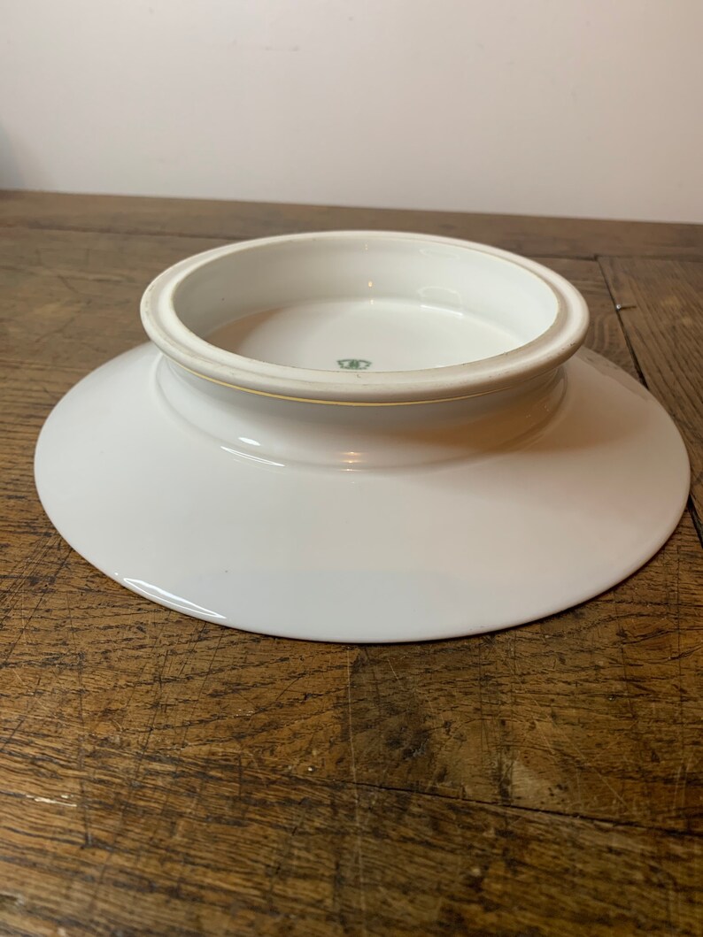 May include: White ceramic pedestal plate with a raised centre and a green mark on the bottom.