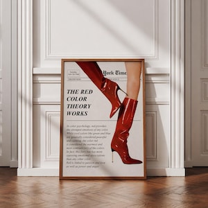 Peut inclure: Une affiche encadrée avec le texte "THE RED COLOR THEORY WORKS" et une image de bottes à talons hauts rouges. L'affiche est dans un cadre en bois et est appuyée contre un mur blanc et un sol en bois.