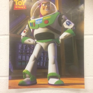 May include: A poster featuring Buzz Lightyear from Disney's Toy Story. Buzz is in his signature white, green, and purple spacesuit, with a clear helmet. The Toy Story logo is visible in the top left corner. The background shows a blurred interior.