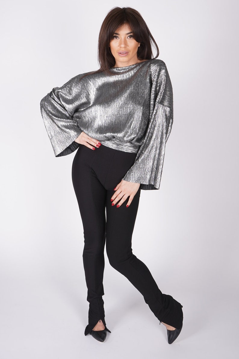 May include: A silver metallic top with long sleeves and a fitted black pair of pants. The model is wearing black shoes.