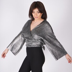 May include: A silver metallic wrap top with long sleeves and a V-neckline. The top is tied at the waist and has a flowing, relaxed fit.