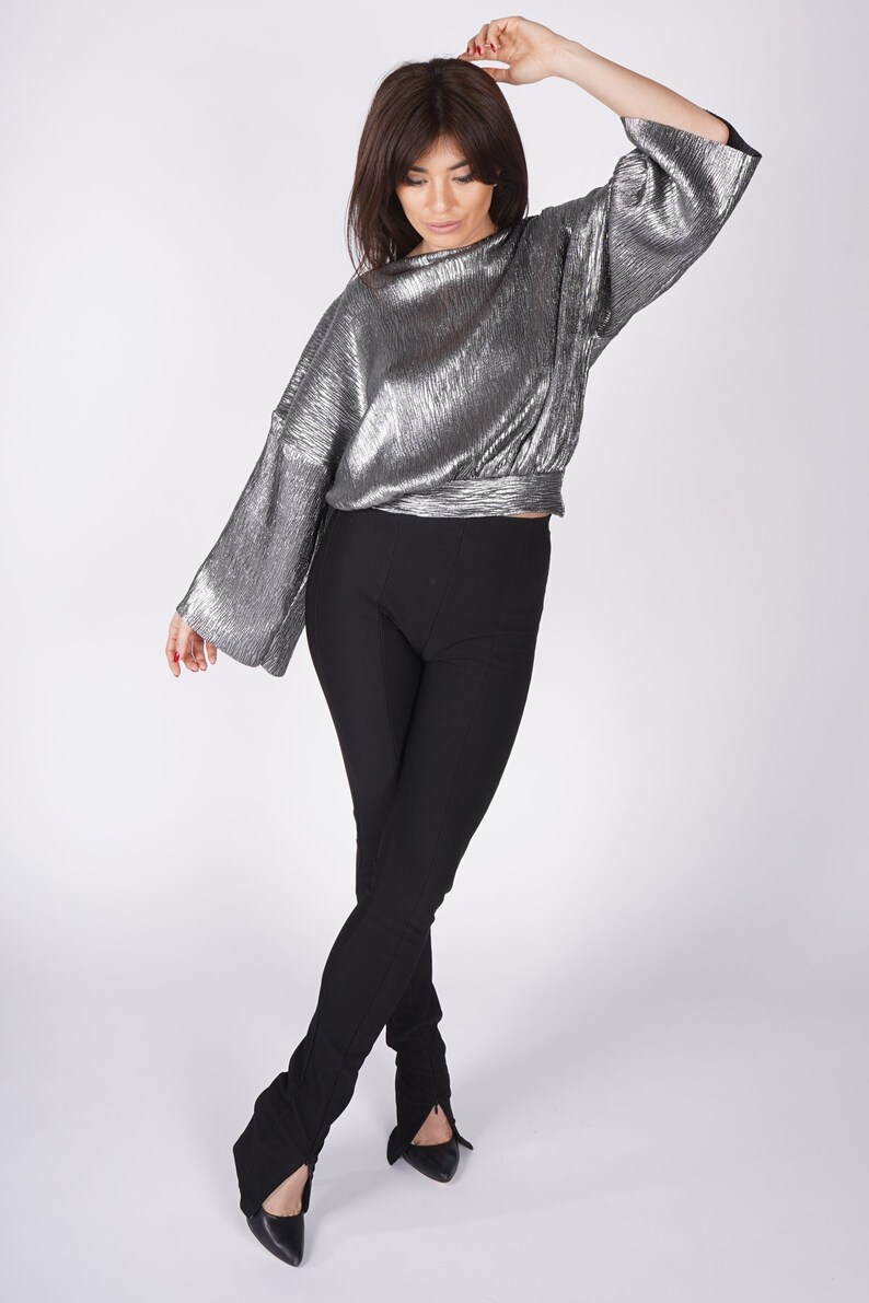 May include: A silver metallic top with long sleeves and a black pair of pants with a wide leg.