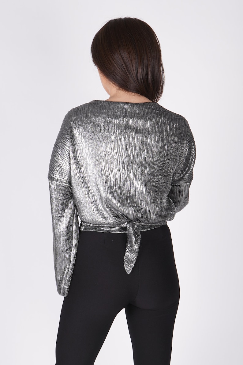 May include: A silver metallic top with long sleeves and a tie at the back. The top is worn with black leggings.