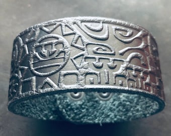 Op de afbeelding: Een zilveren leren armband met een reliëf geometrisch patroon. De armband is gemaakt van echt leer en heeft een zilveren afwerking.