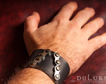 May include: A black leather bracelet with a silver chain detail. The bracelet is worn on a person's wrist.
