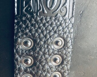 Op de afbeelding: Close-up van een zwarte leren armband met zilveren metalen studs. De armband heeft een decoratief reliëfdesign.