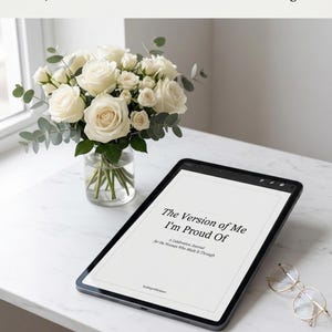 Peut inclure: Une tablette numérique affiche le texte "The Version of Me I'm Proud Of" avec un bouquet de roses blanches dans un vase en verre. Des lunettes à monture dorée sont posées sur la table. Le journal est décrit comme "A Celebration Journal for the Woman Who Made It Through."
