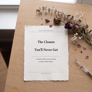 Peut inclure: Un journal intitulé "The Closure You'll Never Get" sur une surface en bois. La couverture du journal est en papier texturé blanc cassé avec le texte "HEALINGWITHROSECO" et "ROSE EDITIONS". Des fleurs séchées et un stylo sont disposés autour du journal.