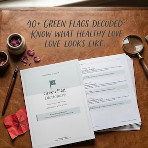 Puede incluir: Un libro abierto titulado "Green Flag Dictionary" con el texto "40+ Green Flags Decoded: Know What Healthy Love Looks Like." El libro está sobre una superficie de cuero marrón, con un bolígrafo, una lupa y pequeños cuencos cerca.