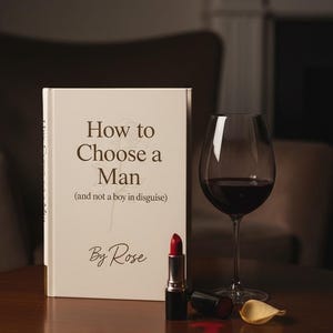 May include: A book titled "How to Choose a Man (and not a boy in disguise)" by Rose, a glass of red wine, and a red lipstick on a wooden table. A lipstick tube and a petal are also on the table.