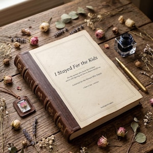 Peut inclure: Un journal intitulé "I Stayed For the Kids" avec une couverture en cuir marron et un stylo doré. Le journal est entouré de fleurs séchées et d'un petit pendentif avec une rose préservée, sur une surface en bois.