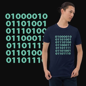Op de afbeelding: Een donkerblauw t-shirt met een patroon van tealblauwe binaire code. De code luidt "01000010 01110100 01110100 01100011 01101111 01110100 01110001 01101110".
