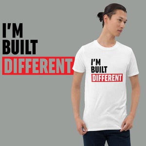 Könnte beinhalten: Weißes T-Shirt mit schwarzem Text, der "I'm Built Different" in Rot lautet.