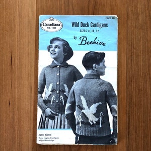 May include: A vintage knitting pattern booklet for Wild Duck Cardigans by Beehive, featuring a photo of two children wearing the cardigans. The pattern is for sizes 8, 10, and 12. The booklet is titled "Canadiana No. 1005" and the price is 25¢.