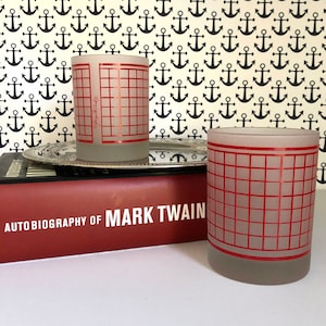 May include: Two frosted glass tumblers with a red grid pattern. The tumblers are sitting on a silver tray and a red book with the text "Autobiography of Mark Twain".