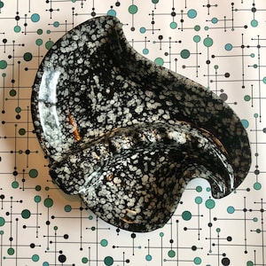 Peut inclure: Cendrier en céramique noir et blanc avec un motif moucheté. Le cendrier est en forme de vague et a un bol large et peu profond.