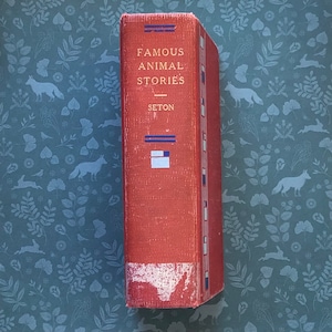 May include: A red hardback book titled "Famous Animal Stories" by Seton. The book has a blue and white striped design on the spine.