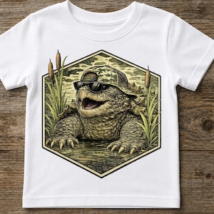 Könnte beinhalten: Weißes T-Shirt mit einer Cartoon-Schnappschildkröte, die eine Sonnenbrille und einen Camouflage-Hut trägt. Die Schildkröte befindet sich im Wasser mit Schilf auf beiden Seiten, eingebettet in einen sechseckigen Rahmen. Das T-Shirt besteht aus einem weichen, bequemen Material.