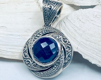 Peut inclure: Un pendentif en argent avec un design complexe mettant en valeur une pierre précieuse bleu foncé au centre.