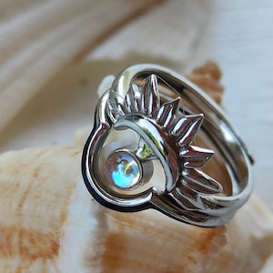 Può includere: Un anello d'argento con un designo a forma di sole e luna e una pietra preziosa iridescente al centro.