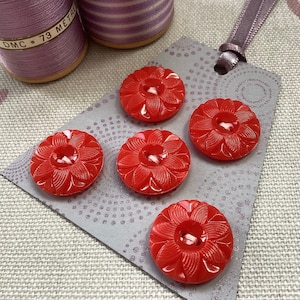 May include: Five red plastic buttons with a flower design. The buttons are arranged in a semi-circle on a grey card with white polka dots.